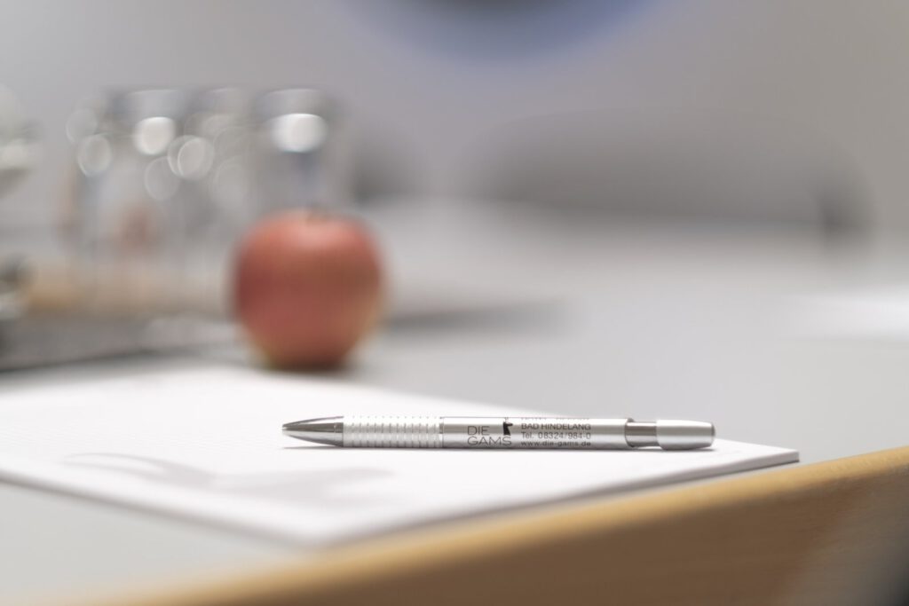 Close-up of a prepared place in the conference room of Die Gams Hotel Resort in Bad Hindelang with branded ballpoint pen, notepad and fresh apple.