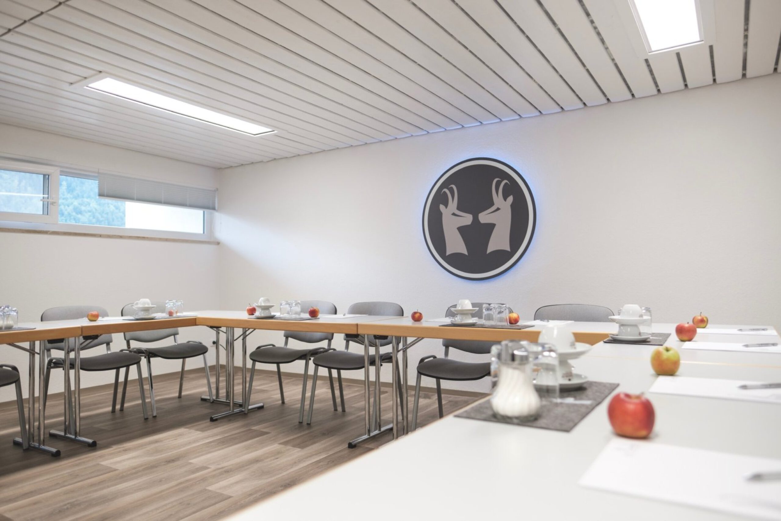Heller Tagungsraum im Die Gams Hotel Resort in Bad Hindelang mit U-förmiger Bestuhlung, Tagungsmaterial, Getränken und beleuchtetem Gams-Logo an der Wand.