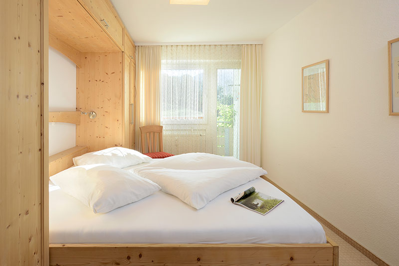 Helles Schlafzimmer in der Ferienwohnung des Die Gams Hotel Resort in Bad Hindelang mit Doppelbett, Einbauschrank aus Holz und Zugang zum Balkon.