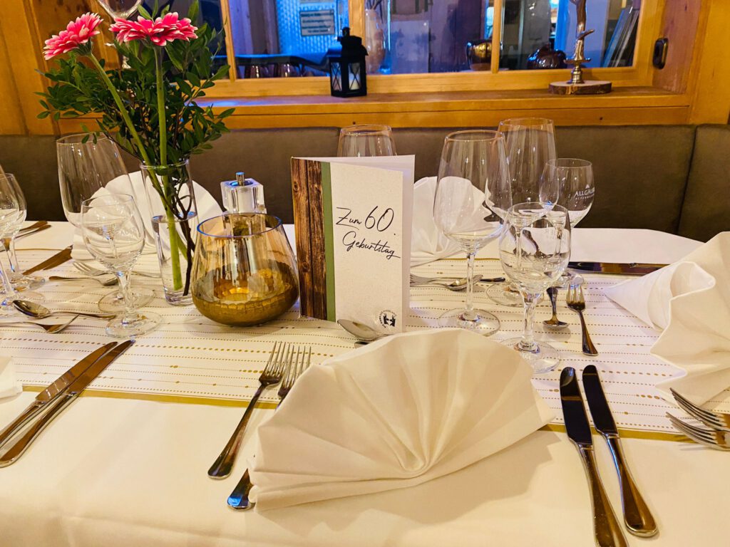 Festively set table at the Die Gams Hotel Resort in Bad Hindelang for a birthday party with flowers, candles, menu cards and elegantly folded napkins.