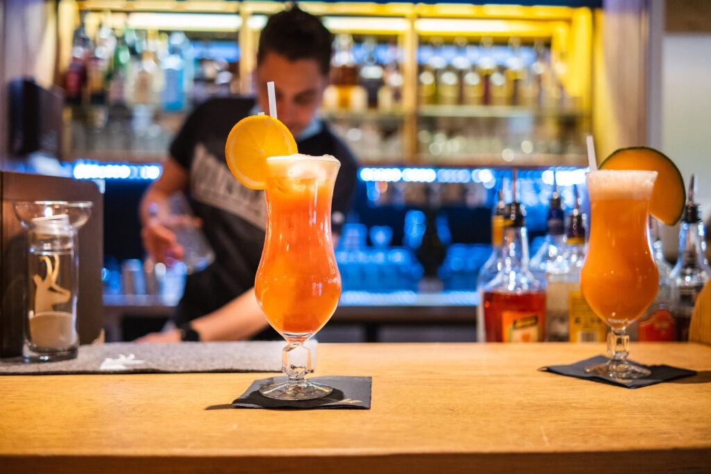 Fruity cocktails at the hotel bar of the Die Gams holiday resort in Bad Hindelang with a bartender in the background and a cozy evening atmosphere.