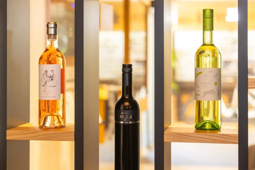 Stilvolle Weinpräsentation im Die Gams Hotel Resort in Bad Hindelang mit erlesenen Flaschen Rosé, Rot- und Weißwein in beleuchtetem Holzregal.