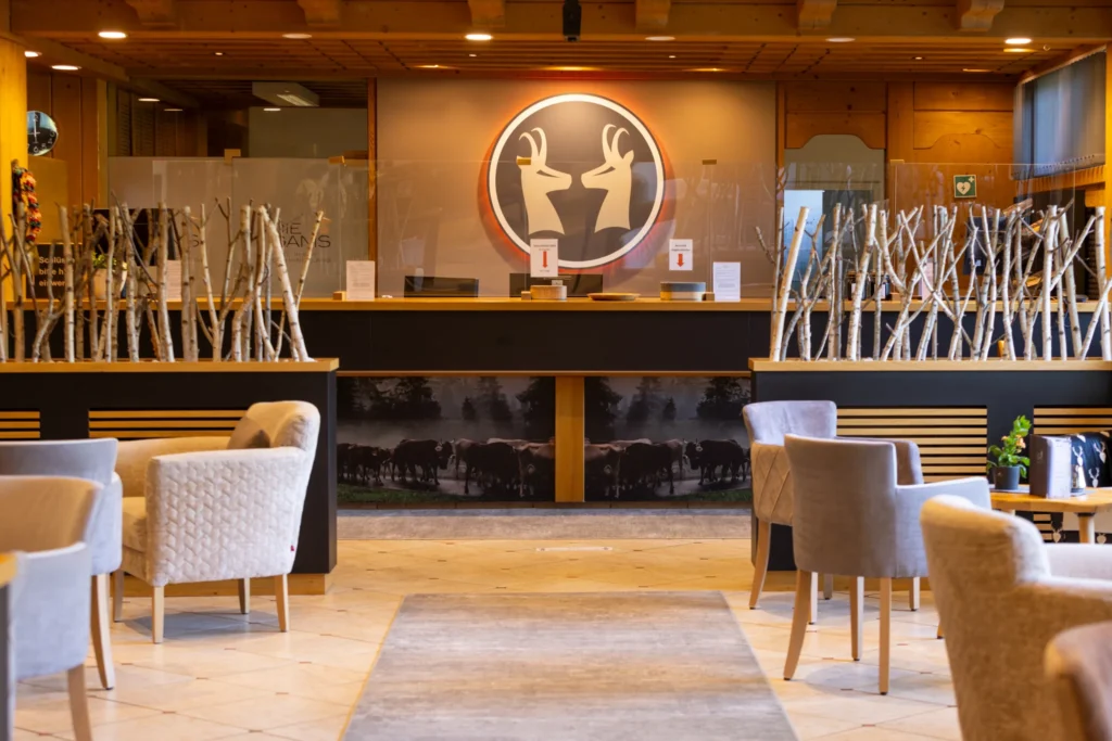 Heller Empfangsbereich des Die Gams Hotel Resort in Bad Hindelang mit gemütlichen Sitzgelegenheiten, Naturdeko aus Birkenholz und markantem Gams-Logo.