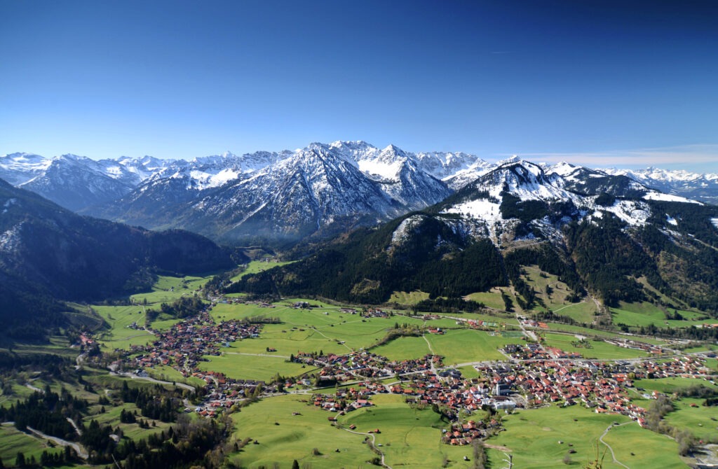 Aktivurlaub in Bad Hindelang - Panoramablick auf Bad Hindelang im Allgäu mit malerischem Tal, verschneiten Alpen und tiefblauem Himmel.