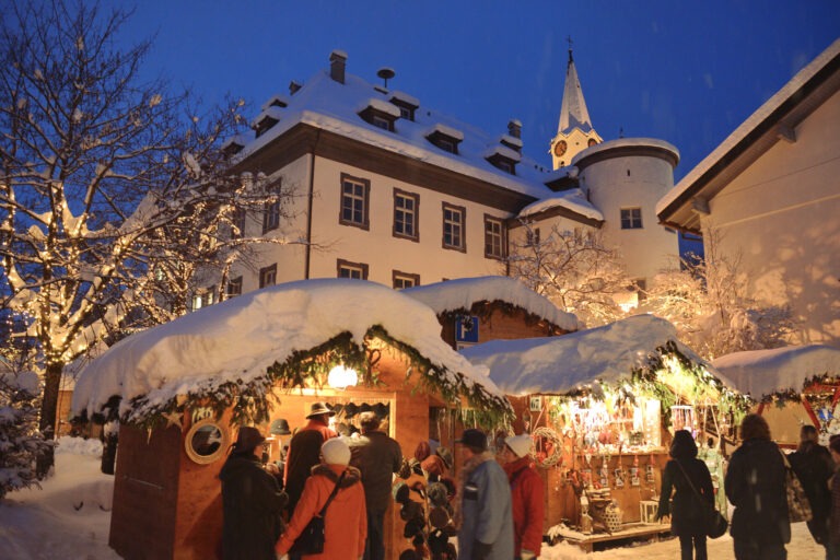 Atmospheric Christmas market in Bad Hindelang in the Allgäu with festively decorated wooden huts, fairy lights and a snowy backdrop in the evening.