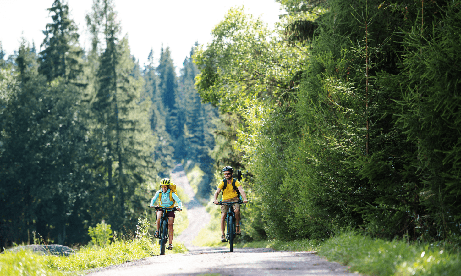 Zwei Urlauber beim E-Biken auf einem Waldweg in den Allgäuer Alpen bei Bad Hindelang – umgeben von grüner Natur und sommerlicher Berglandschaft.