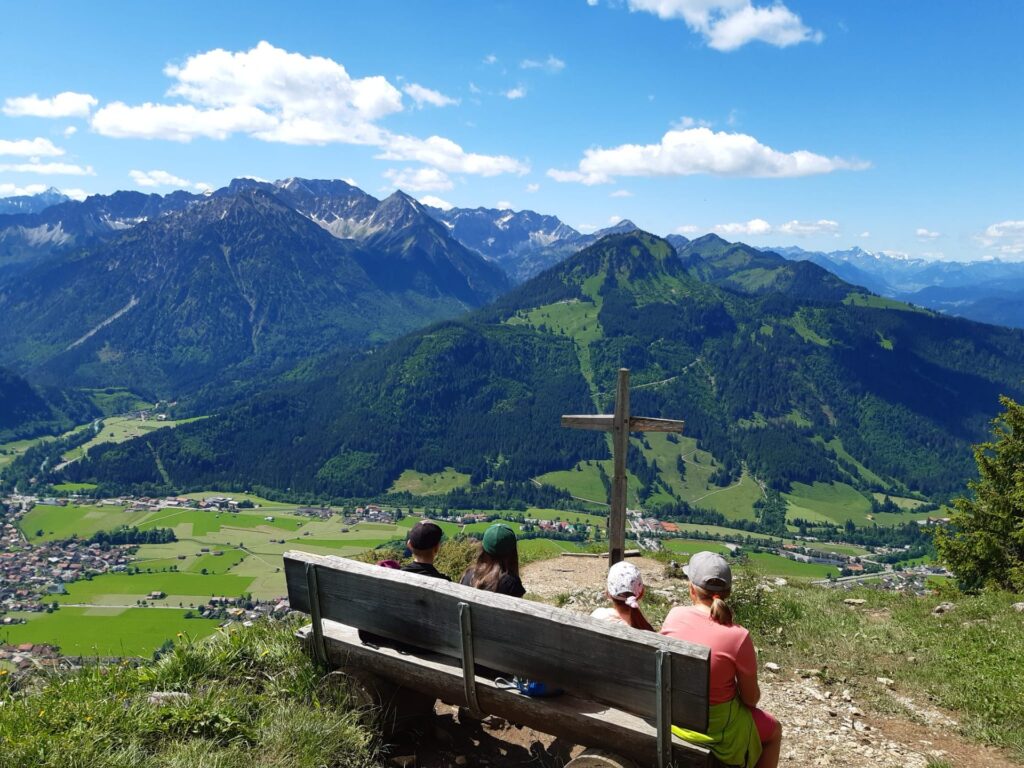 Wanderer rasten am Gipfelkreuz mit Blick über Bad Hindelang