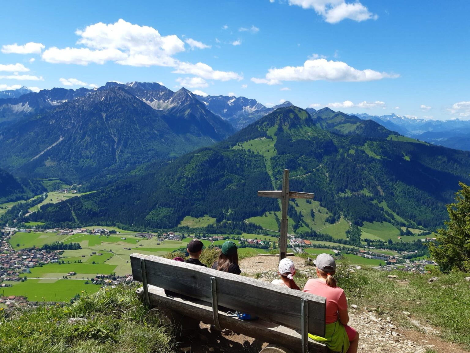 Wanderer rasten am Gipfelkreuz mit Blick über Bad Hindelang