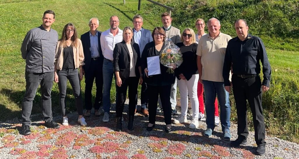 Elisabeth Bichler mit Urkunde und Blumenstrauß inmitten des GAMS-Teams auf einer Wiese in Bad Hindelang