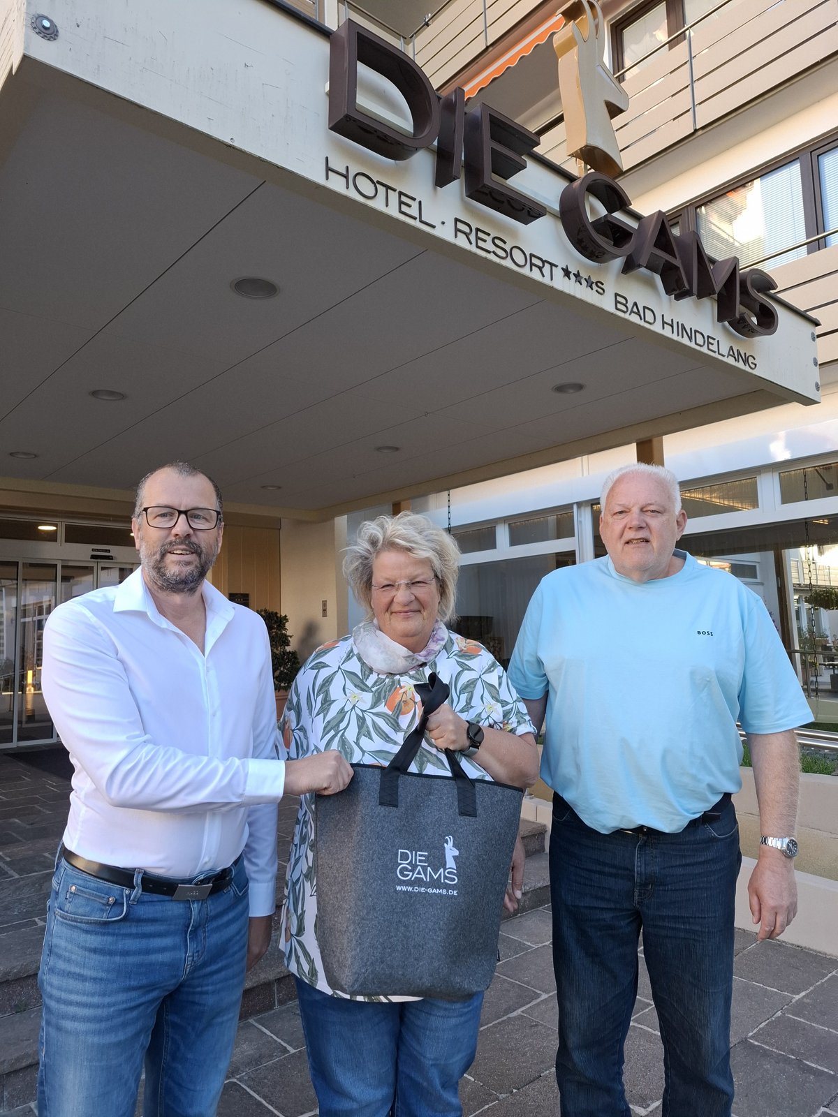 Ehepaar Placzek mit GAMS-Geschenktasche vor dem Hoteleingang der GAMS in Bad Hindelang