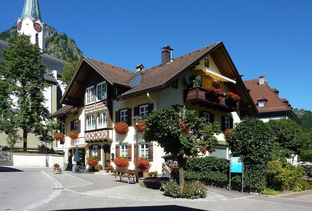 Bemalte Häuser mit Blumenbalkonen an der Marktstraße in Bad Hindelang, dahinter der Kirchturm