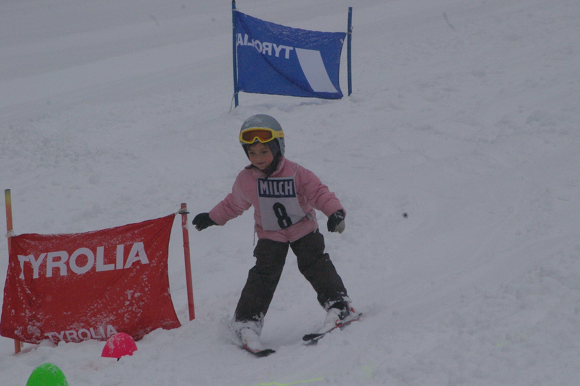 Kind mit Helm und Skibrille fährt im Pflug durch ein Tor bei einem Kinderskirennen