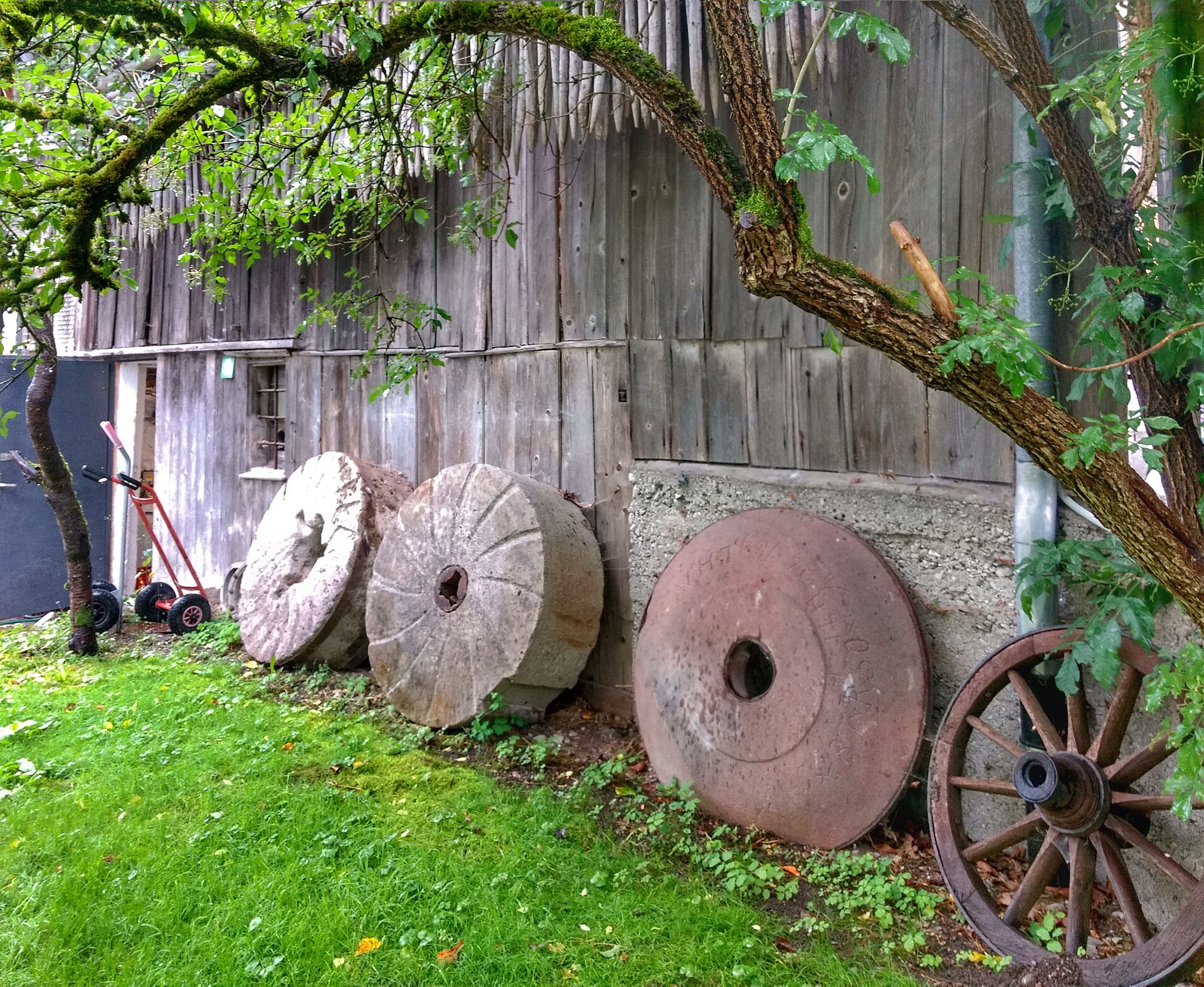 Alte Mühlsteine und Wagenrad vor dem Holzgebäude der Oberen Mühle in Bad Oberdorf