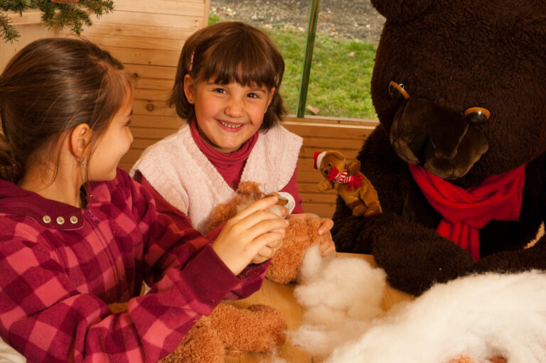 Zwei lachende Mädchen mit Plüschtieren auf dem Kinderweihnachtsmarkt