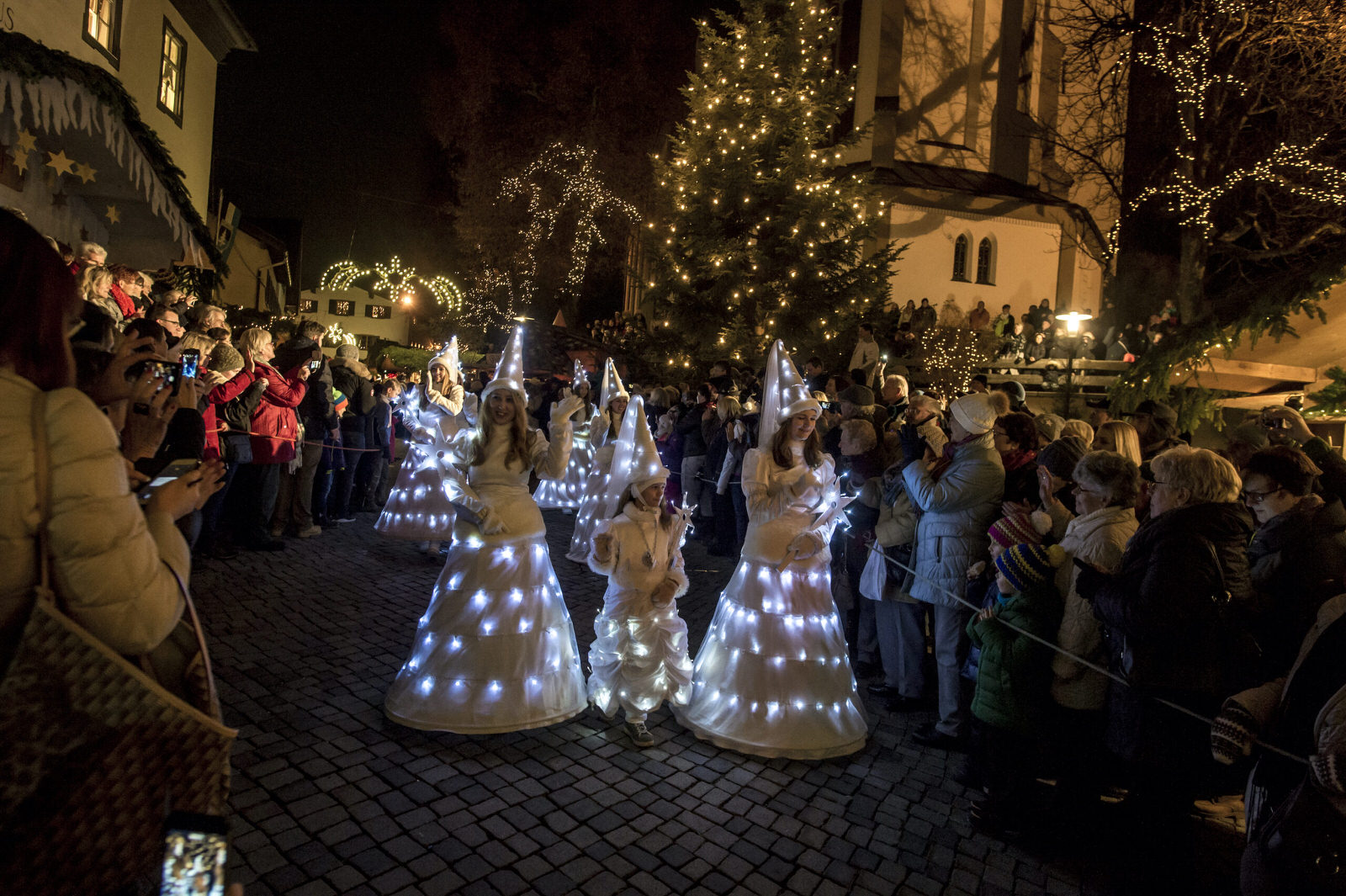 Leuchtende weiße Figuren ziehen beim Weihnachtsumzug durch die Menge