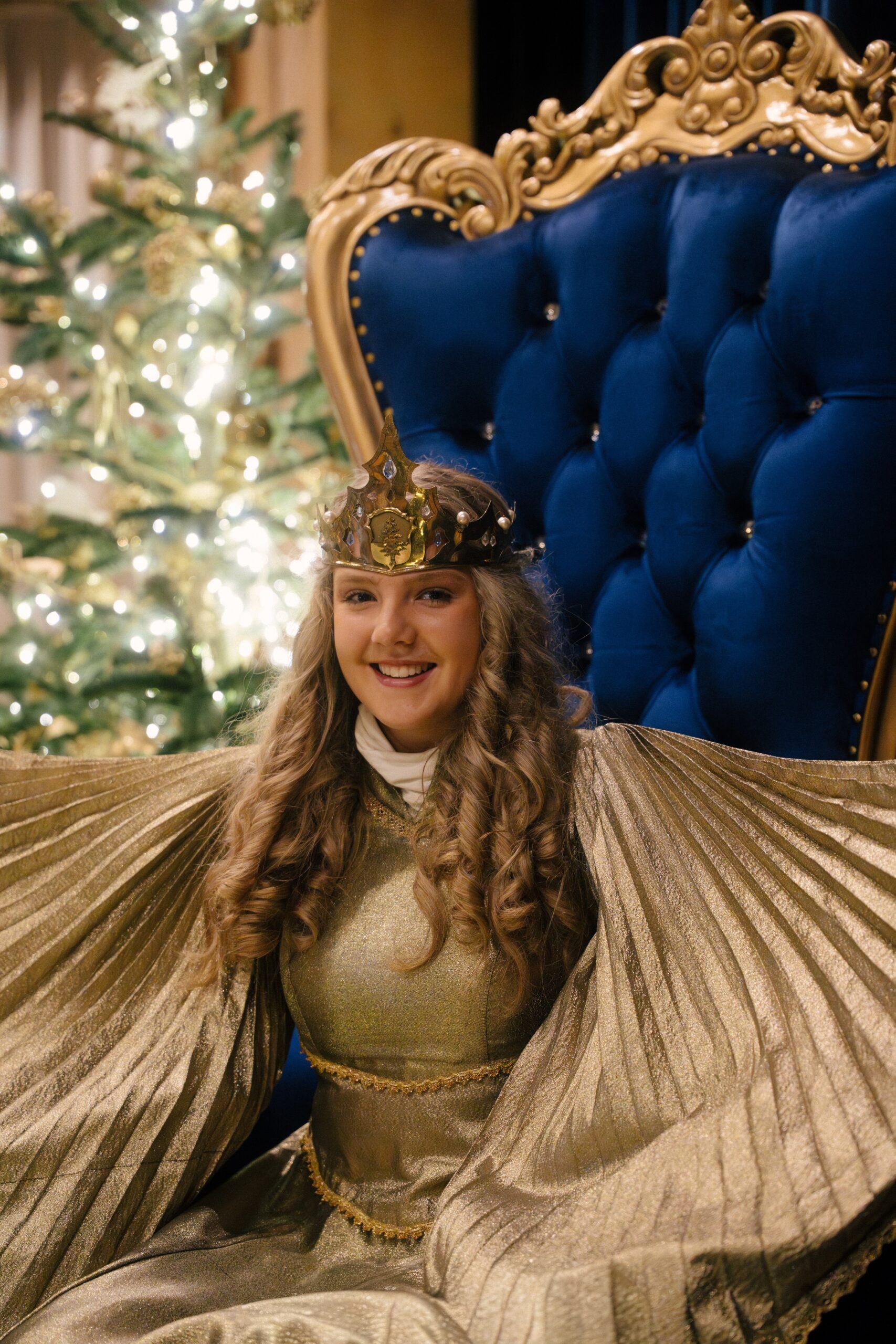 Das Christkind in goldenem Gewand auf einem blauen Thron vor einem Christbaum