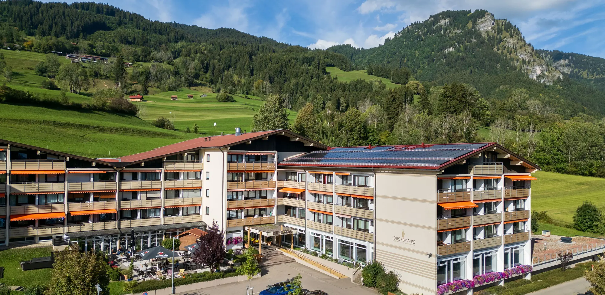 Hotel DIE GAMS aus der Luft mit Haupteingang, Sonnenterrasse und Bergkulisse