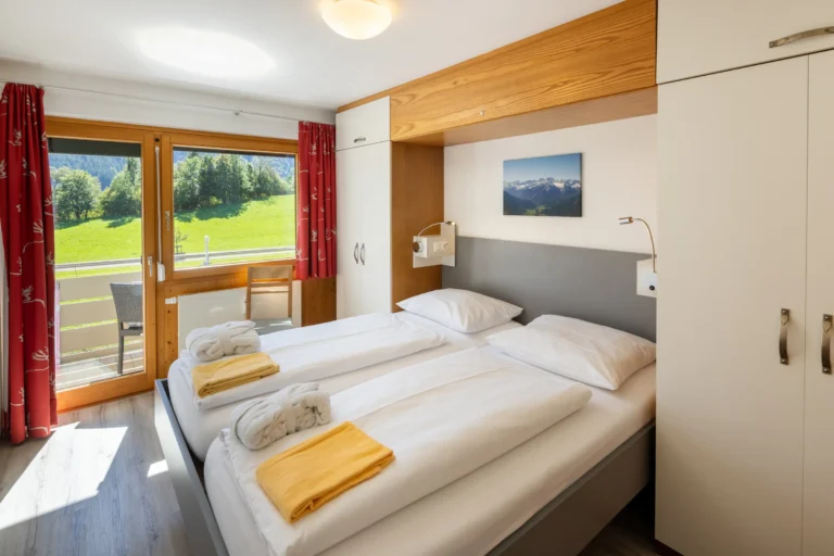 Schlafzimmer mit Doppelbett, rotem Vorhang und Balkontür in einem Premium-Appartement im Hotel DIE GAMS